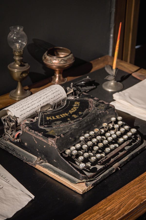 Antique typewriter beside a brass lamp and ink pen